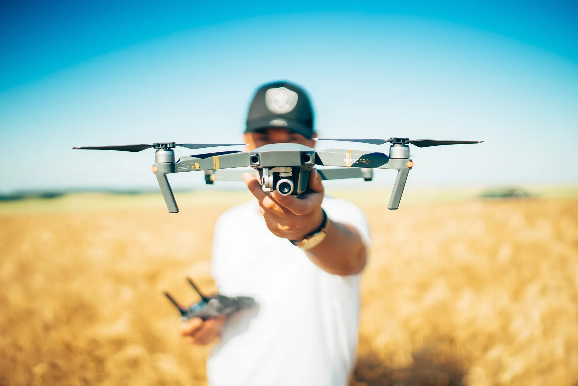 Operator holding a camera drone in front of an open field under a clear sky