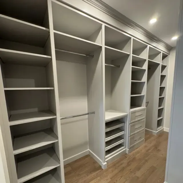 Walk-in closet with tiered open shelving, double hanging rods and built-in drawers beneath a vaulted, crown-molded ceiling