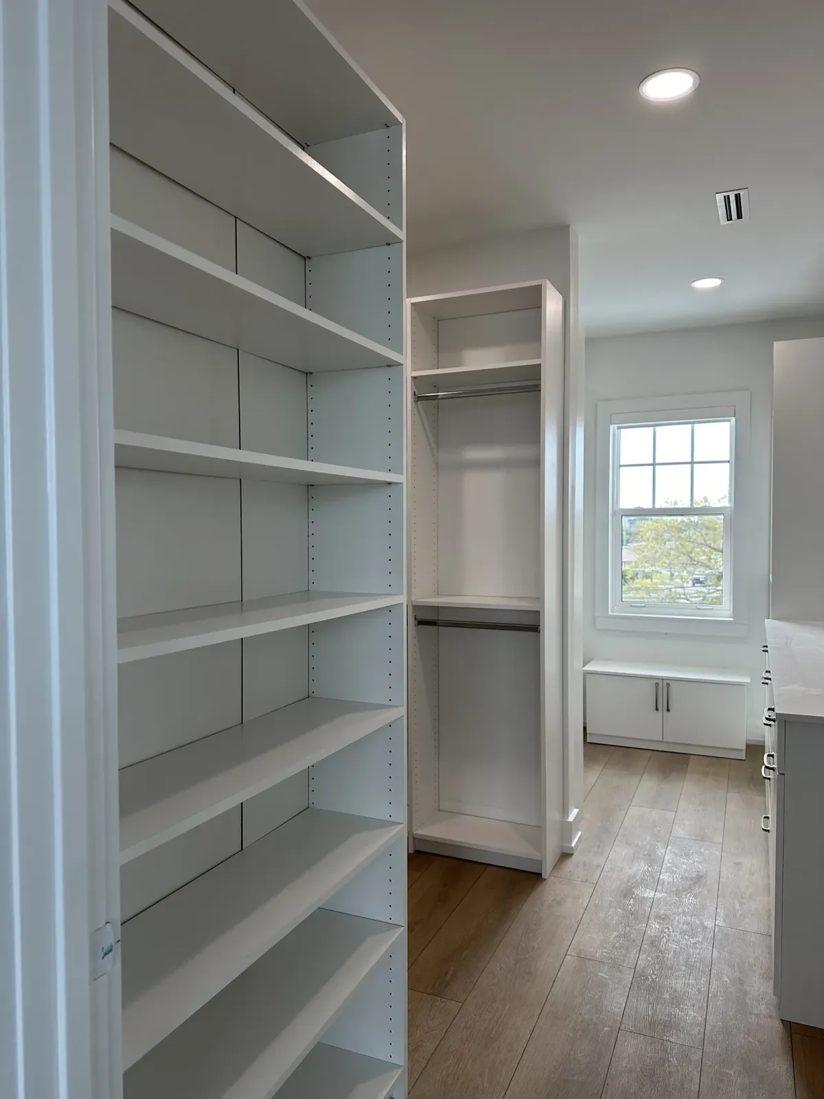 Reach-in closet with open shelving beside a hallway leading to a sunlit window and kitchen counter