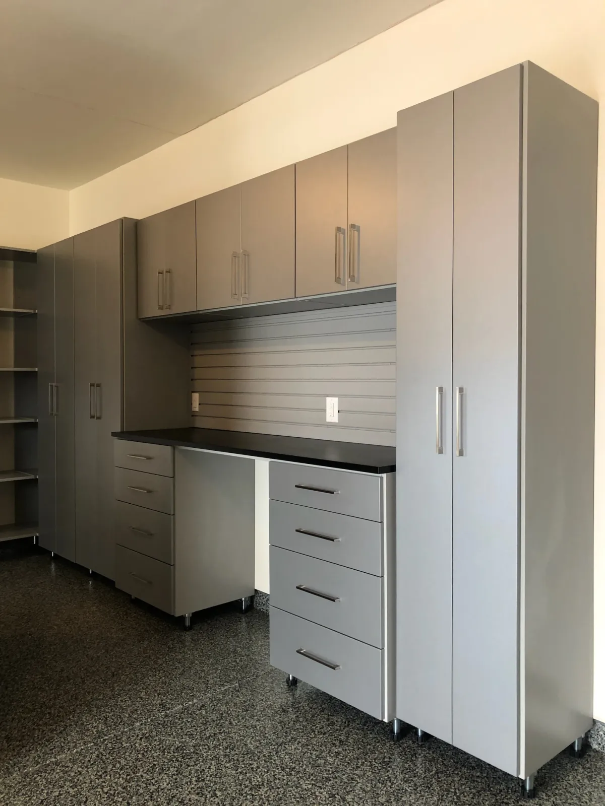 Floor-to-ceiling gray garage cabinetry with a black countertop workstation and slatwall storage panel