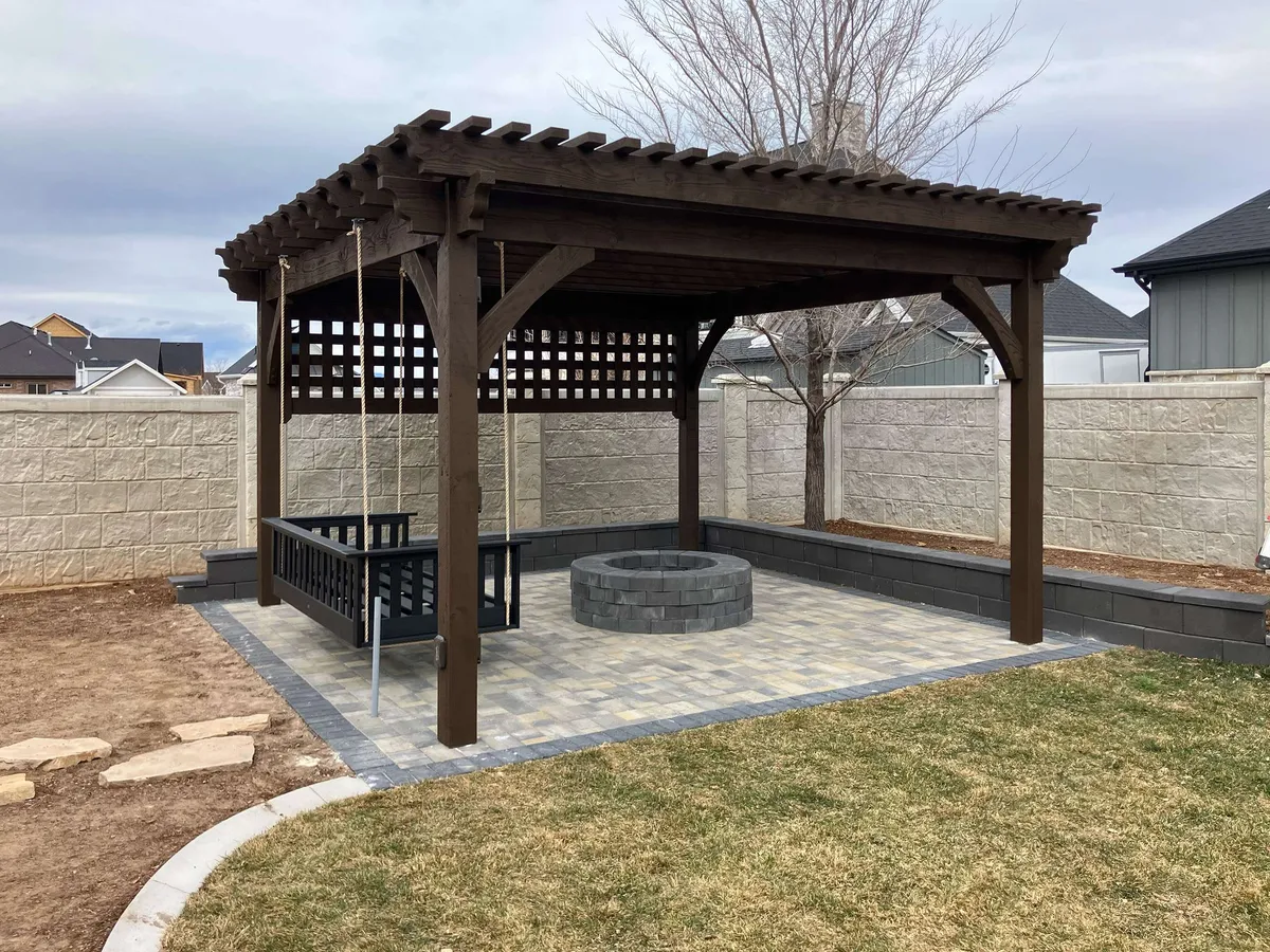 Backyard pergola with a hanging bench swing and paver patio built around a fire pit