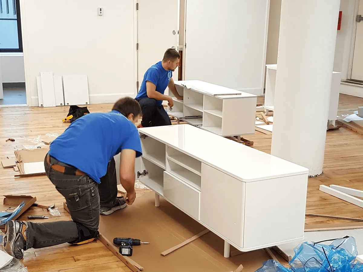 Two technicians assembling a built-in white cabinet and media console